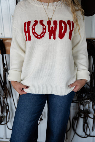 Person wearing a white sweater with 'HOWDY' in red text, standing indoors.