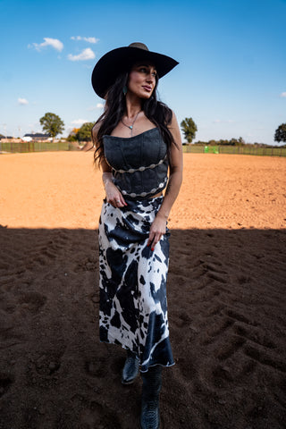 Woman in a black and white cow print dress with a black hat standing in an open field.