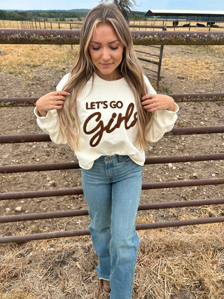 Woman wearing a white sweatshirt with 'Let's Go Girl' text, standing on train tracks.