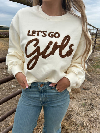 Person wearing a cream-colored sweatshirt with 'Let's Go Girls' text in brown.