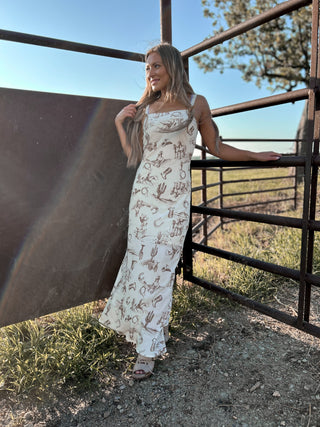 Woman in a patterned dress standing next to a metal gate with a scenic background