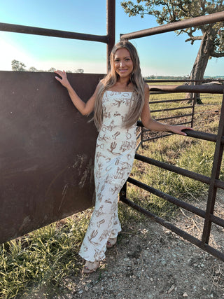 Woman in a cactus-patterned dress standing next to a metal gate with a scenic background.