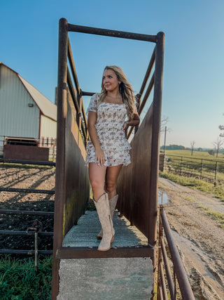 Woman standing on a metal staircase in a rural setting with a barn and open field in the background.