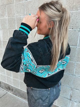 Woman wearing a black jacket with turquoise and white pattern against a stone wall.