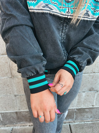 Person wearing a dark jacket with striped cuffs, standing against a stone wall.