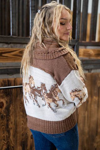Person wearing a brown and white patterned sweater with horse design in a rustic setting.