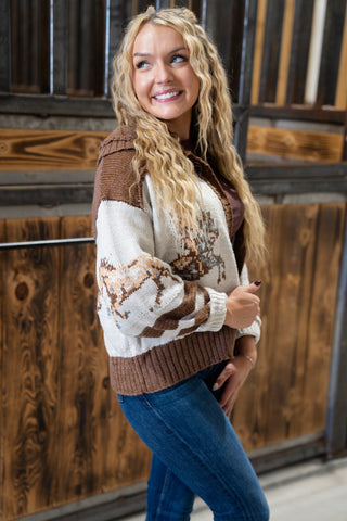 Woman wearing a brown and white patterned sweater standing in front of wooden panels.