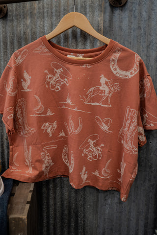 Red shirt with white graphic designs on a wooden hanger against a rustic metal wall.