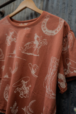 Red shirt with white graphic designs on a wooden hanger against a textured wall.