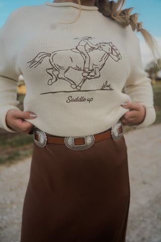 Person wearing a sweater with a horse and rider design and 'Saddle up' text, standing outdoors.
