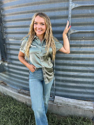 Woman standing against a corrugated metal wall wearing a green shirt and blue jeans.