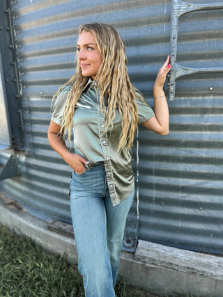 Woman wearing a green shirt and blue jeans standing against a metal wall.