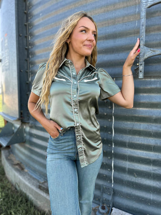 Woman in a green shirt and blue jeans standing next to a metal wall.