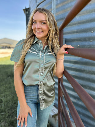Woman in a green shirt and jeans standing next to a metal building.