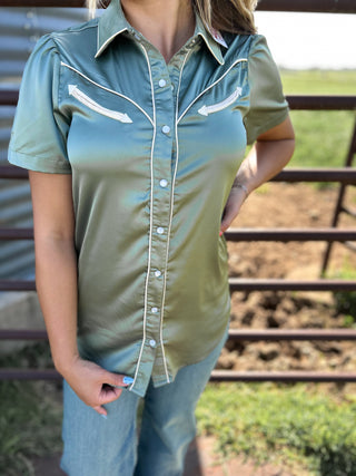 Person wearing a green button-up shirt with white accents in an outdoor setting.