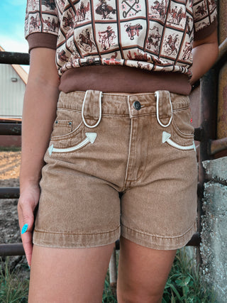 Person wearing a patterned shirt and brown shorts with unique button design.