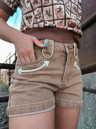 Person wearing brown shorts with white stitching details, standing outdoors.