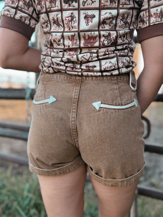 Person wearing a patterned shirt and brown shorts with metal zippers.