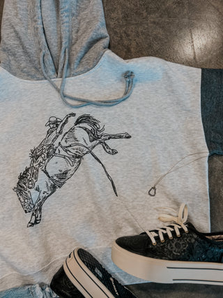 Gray hoodie with a graphic of a person riding a horse, paired with black sneakers on a textured surface.