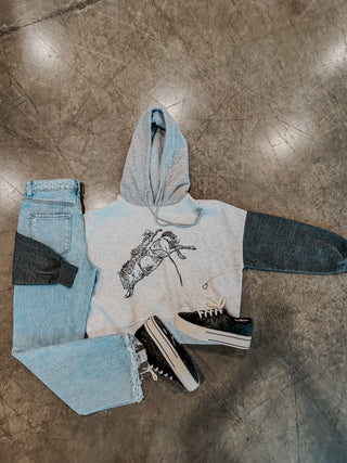 Gray hoodie with graphic design, light blue jeans, and black sneakers on a concrete floor.