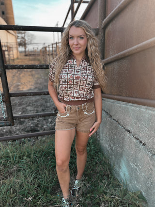 Woman standing in front of a metal gate and wall, wearing a patterned shirt and shorts.