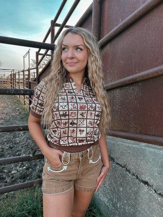 Woman wearing a patterned shirt and shorts standing near a metal fence.