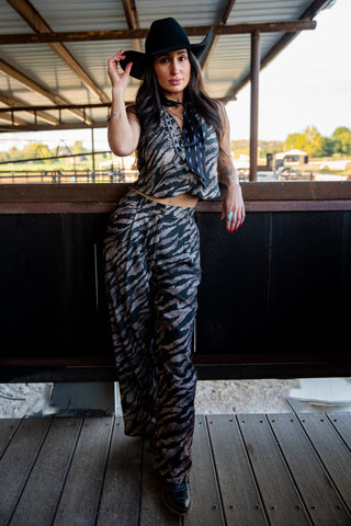 Woman in a zebra print outfit and black hat standing on a wooden deck.