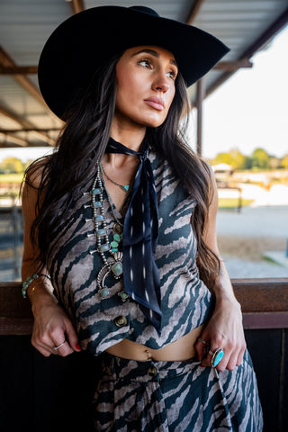 Woman wearing a black hat and patterned outfit with a scenic background
