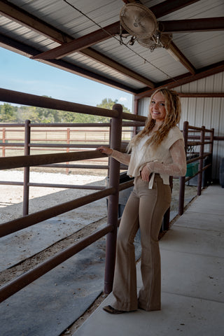 Woman standing inside a barn or stable, wearing a beige outfit.