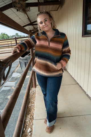 Woman wearing a striped sweater and jeans standing on a porch.