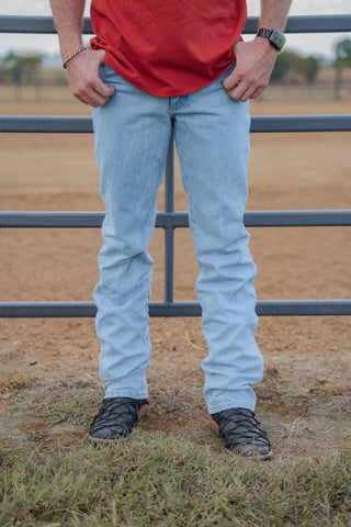 Person wearing light blue jeans and a red shirt standing in front of a metal fence.