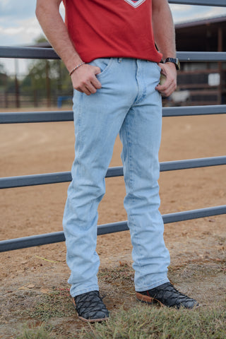 Person wearing a red shirt and light blue jeans standing in an outdoor setting with a metal fence.