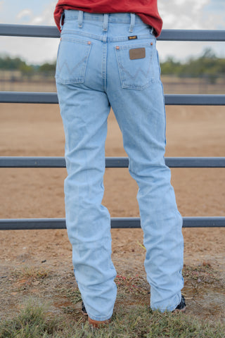 Person wearing light blue jeans standing in front of a metal fence with a blurred natural background