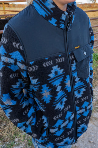 Person wearing a blue and black patterned jacket with a visible brand logo.