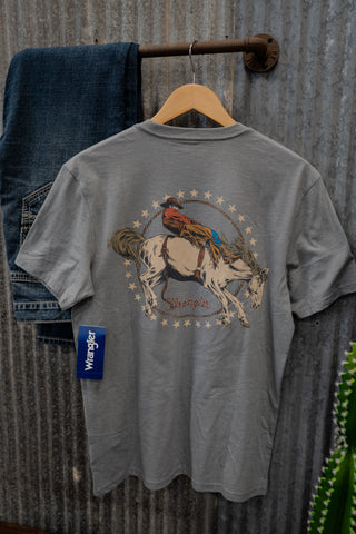 Gray t-shirt with a graphic of a cowboy on a horse, hanging on a wooden hanger against a corrugated metal wall.