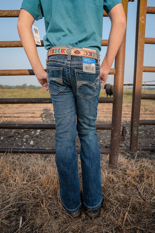 Person wearing blue jeans and a patterned belt standing in a field with a metal fence.