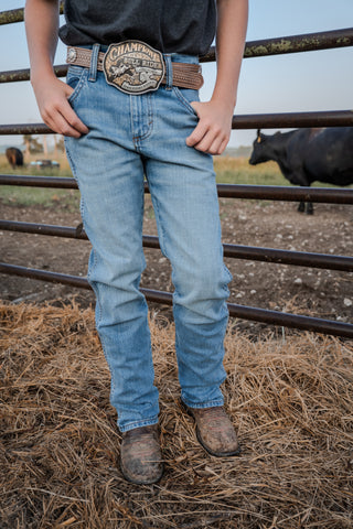 Person wearing blue jeans and a Champion belt buckle in a rural setting with cows in the background.