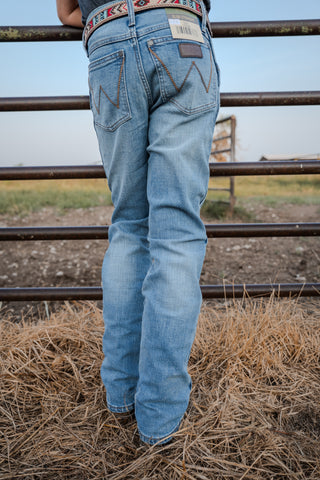 Person wearing light blue jeans standing in a field with a metal fence in the background.