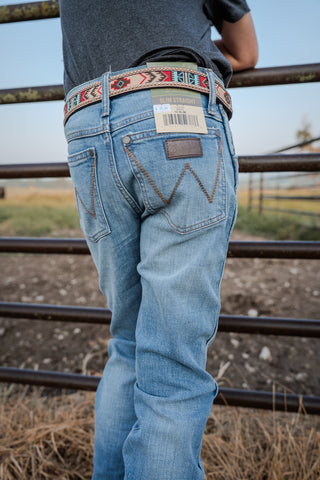Person wearing light blue jeans with a decorative belt, standing near a metal fence.
