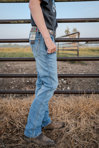 Person wearing blue jeans and a dark shirt standing on hay with a metal fence and grassy field in the background.