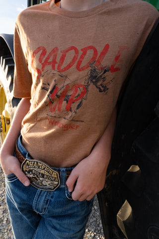 Person wearing a brown t-shirt with graphic design and text, standing outdoors.
