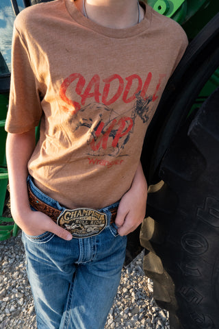 Person wearing a brown t-shirt with graphic design and text, standing next to a vehicle.