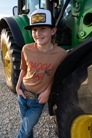 Child wearing a cap and t-shirt standing next to a green tractor