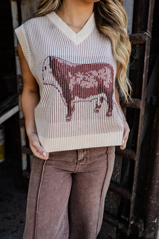 Person wearing a sleeveless sweater with a cow design in a rustic setting
