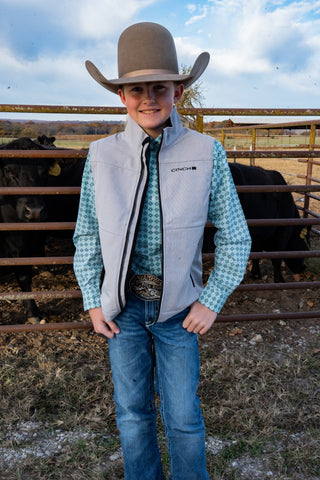Young boy in cowboy attire standing in a barn with cows in the background