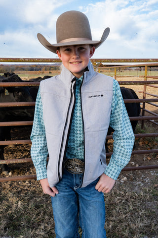 Young boy in cowboy attire standing in a barn with cows in the background