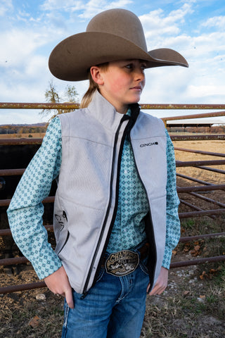 Person wearing a cowboy hat, vest, and patterned shirt in an outdoor setting.