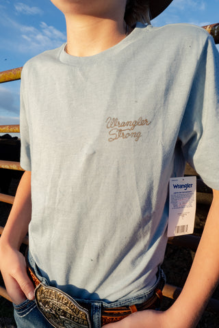 Person wearing a light blue t-shirt with 'Wrangler Strong' text, standing outdoors.