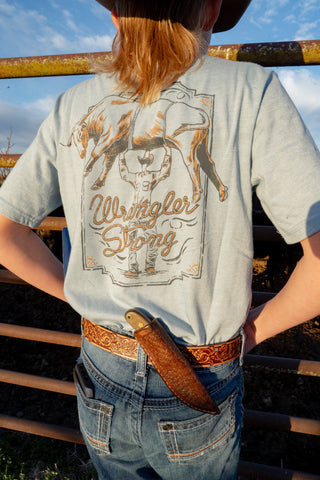 Person wearing a gray t-shirt with a graphic design and text, standing outdoors.